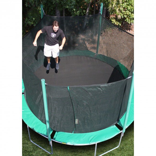 A man in his twenties jumps on a green trampoline.