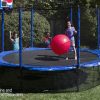 A young girl jumps on a trampoline with safety skirt while mother and brother watch from grass