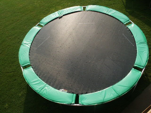 A green trampoline without safety net, in rain on lush green grass