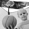 A little blond girl holds a basketball next to a trampoline basketball hoop