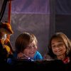 Two kids and a stuffed fox use a flashlight read while camping in their trampoline tent