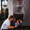 Three kids and their dad read a book in the door of a Vuly tent