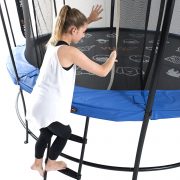 A girl in white tank top and black yoga pants climbs a ladder into a trampoline