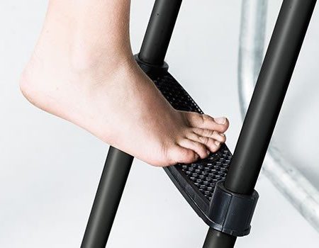 An adult barefoot steps on the second step of a black ladder