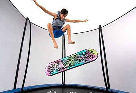 A boy jumps above a colorful trampoline skate deck