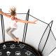 Girl in grey pants and white shirt flails her arms as she jumps on a tramp