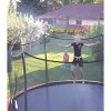 A young girl on a trampoline gets sprayed by a mist sprayer while her younger brother watches