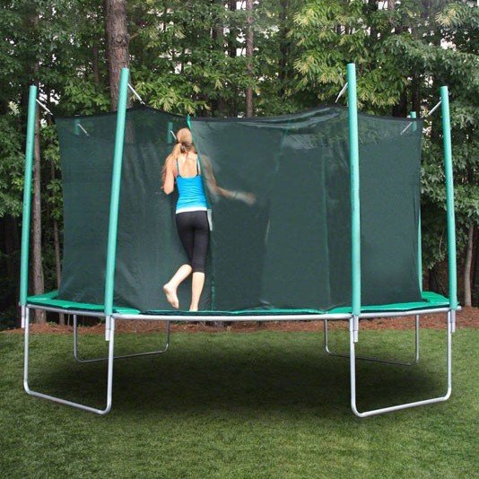 An attractive teenage girl with blue tank top, black yoga pants, and ponytail enters a trampoline safety enclosure.