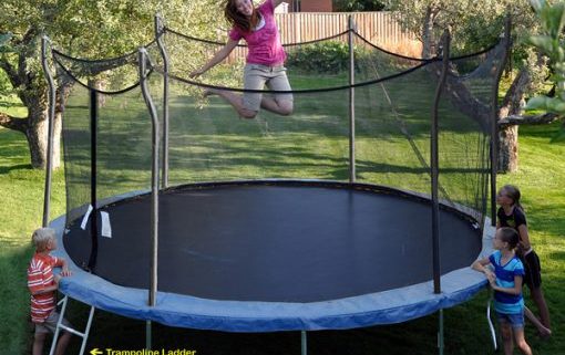 Brunette mom, with kids watching, jumps on a blue Propel Trampoline in backyard