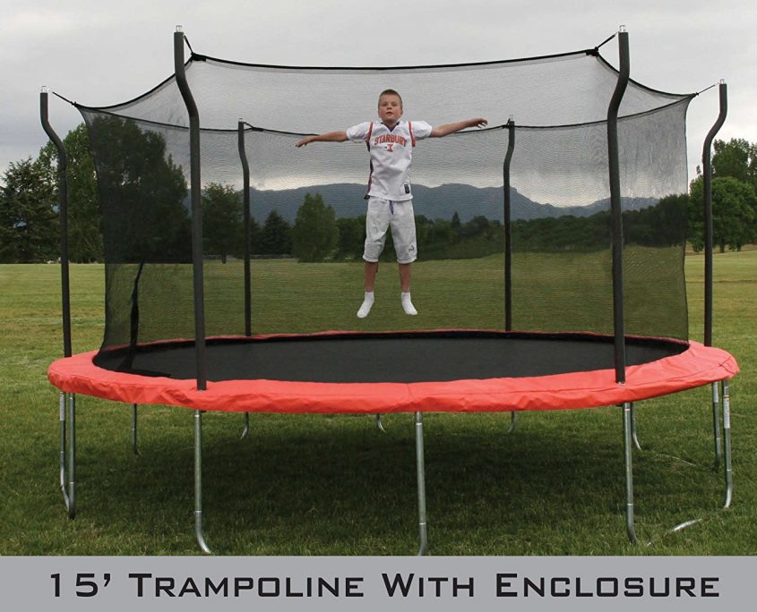 Young boy jumps on 15 foot trampoline with enclosure in grassy field