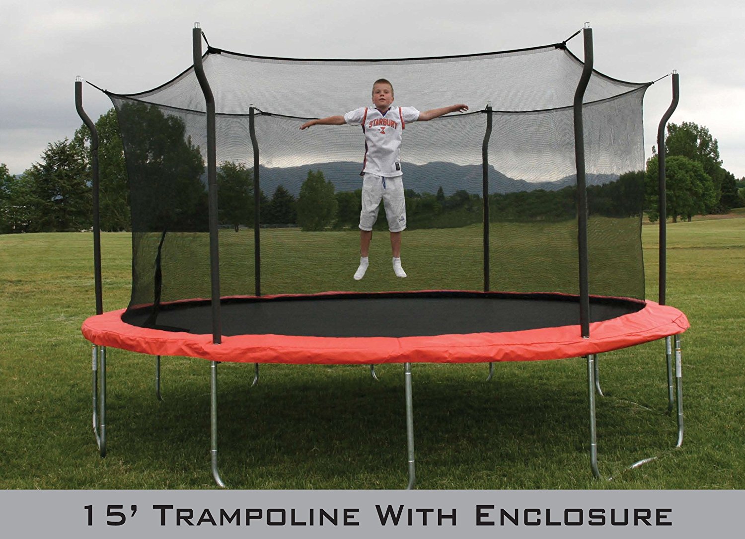 Young boy jumps on 15 foot trampoline with enclosure in grassy field