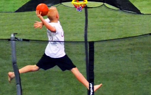 A 10-year old boy jumps to slam dunk his trampoline basketball hoop in his backyard