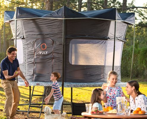 A dad plays with dog and son while mom and daughters eat all while camping