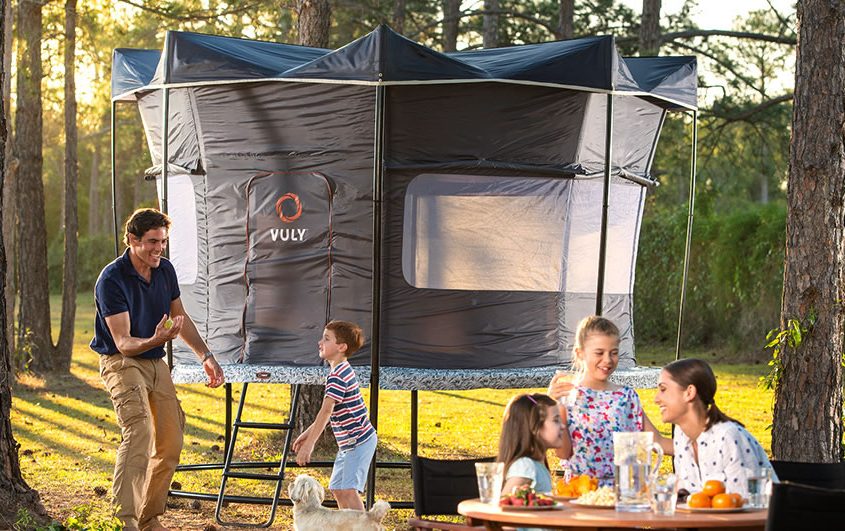 A dad plays with dog and son while mom and daughters eat all while camping