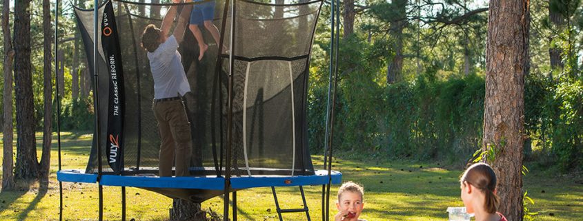 A dad stands on a trampoline holding his son in the air