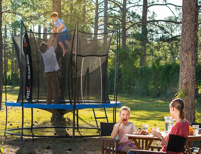 A dad stands on a trampoline holding his son in the air