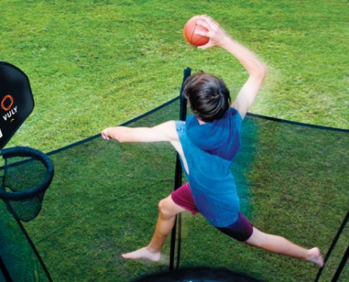 a young boy in blue shirt dunking his Vuly basketball hoop high above his Vuly 2 trampoline